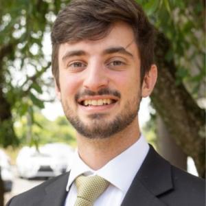 Mitchell Kurek wearing a suit and green tie smilng outside with trees.