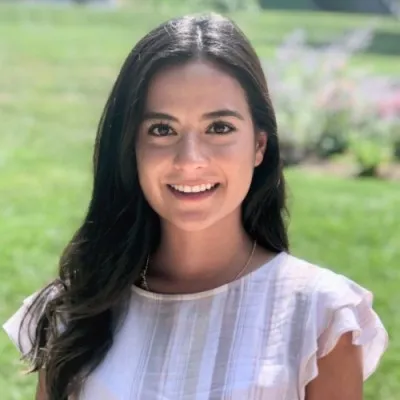 Marilyn Perez-Mendoza wearing a white blouse smiling outside with grass behind her.