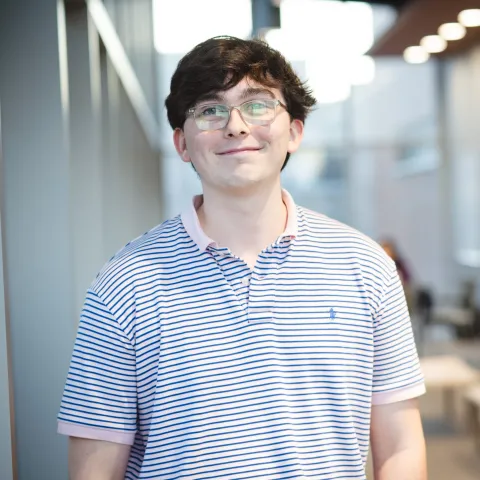 Charles Gaffney standing for his headshot wearing glasses and a striped polo shirt.