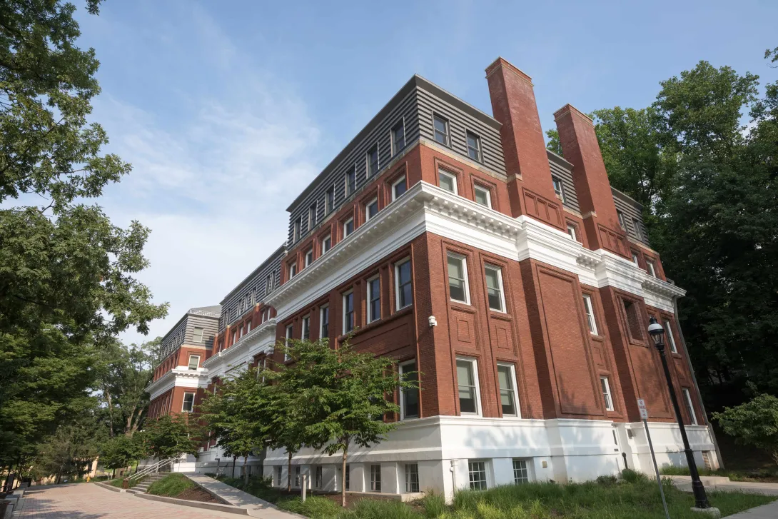 A brick building with chimneys surrounded by green trees.